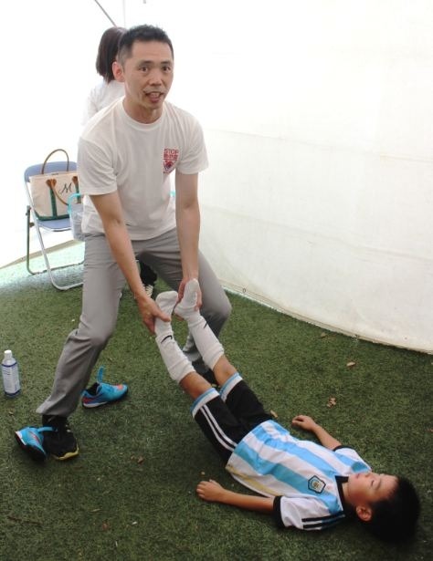 日本アスリートセラピスト協会の水野聰氏が、子どもの協力を得て、リラックス方法を実践しているところ